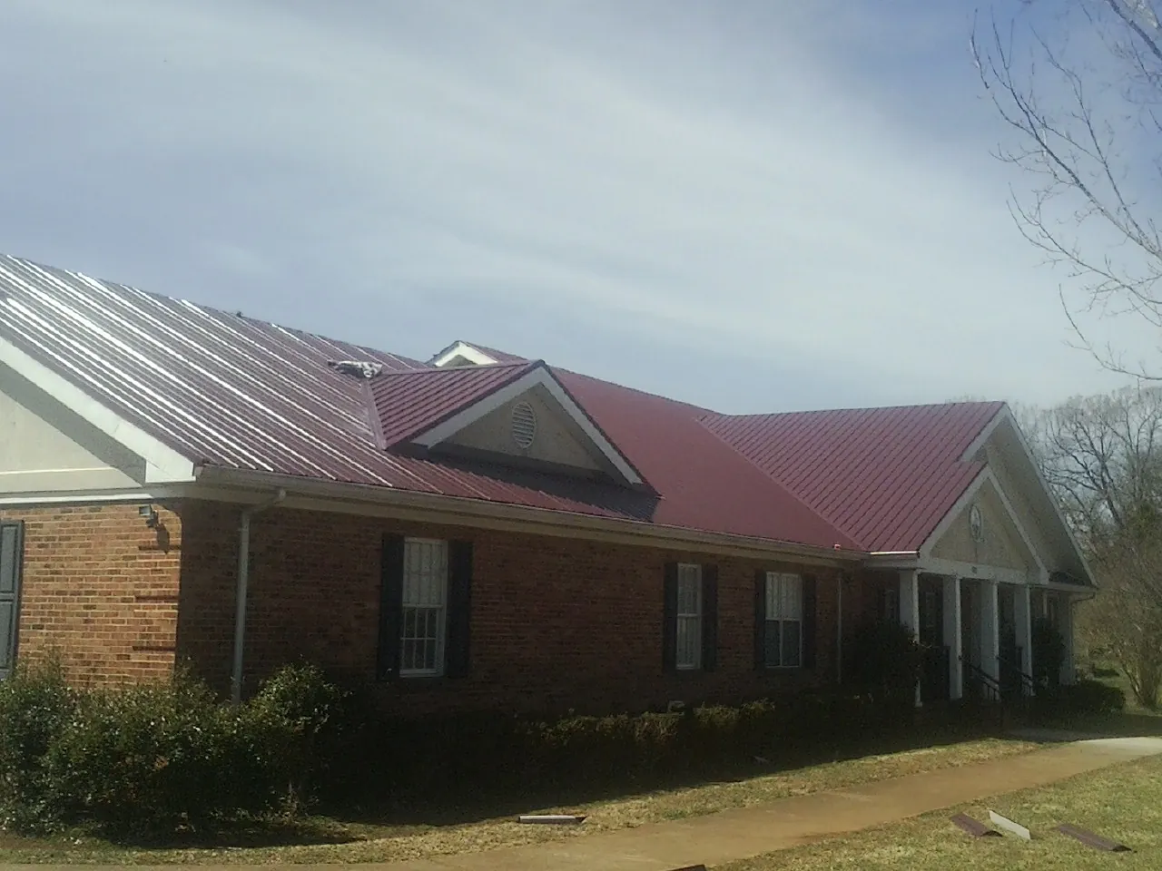 Red metal roof with gabled entries on a long brick building, from a Hail Damage Roof Repair job in Valley Center