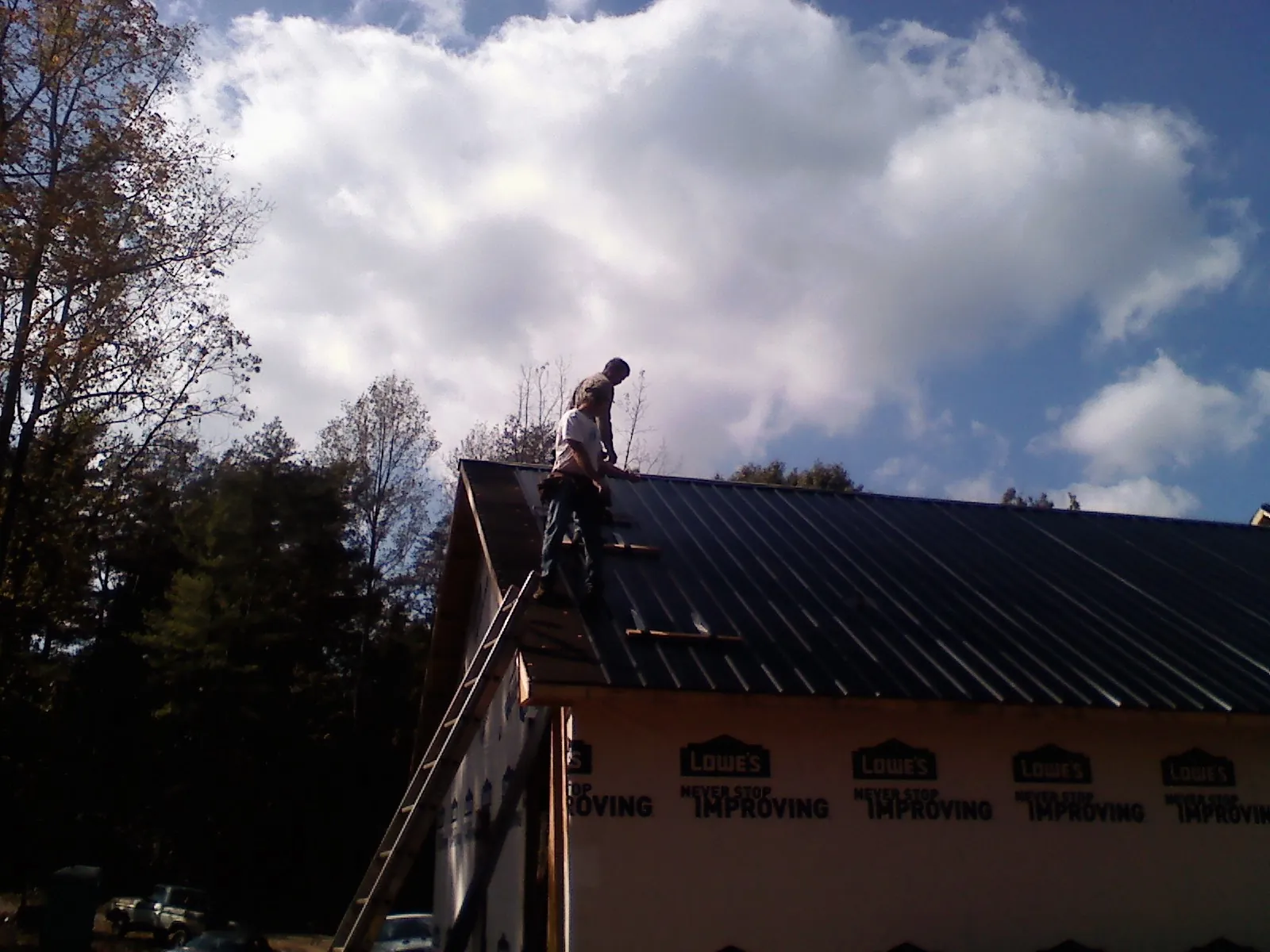 Roofer fastening dark metal panels high against a cloudy sky, from a Roof Inspection job in Valley Center