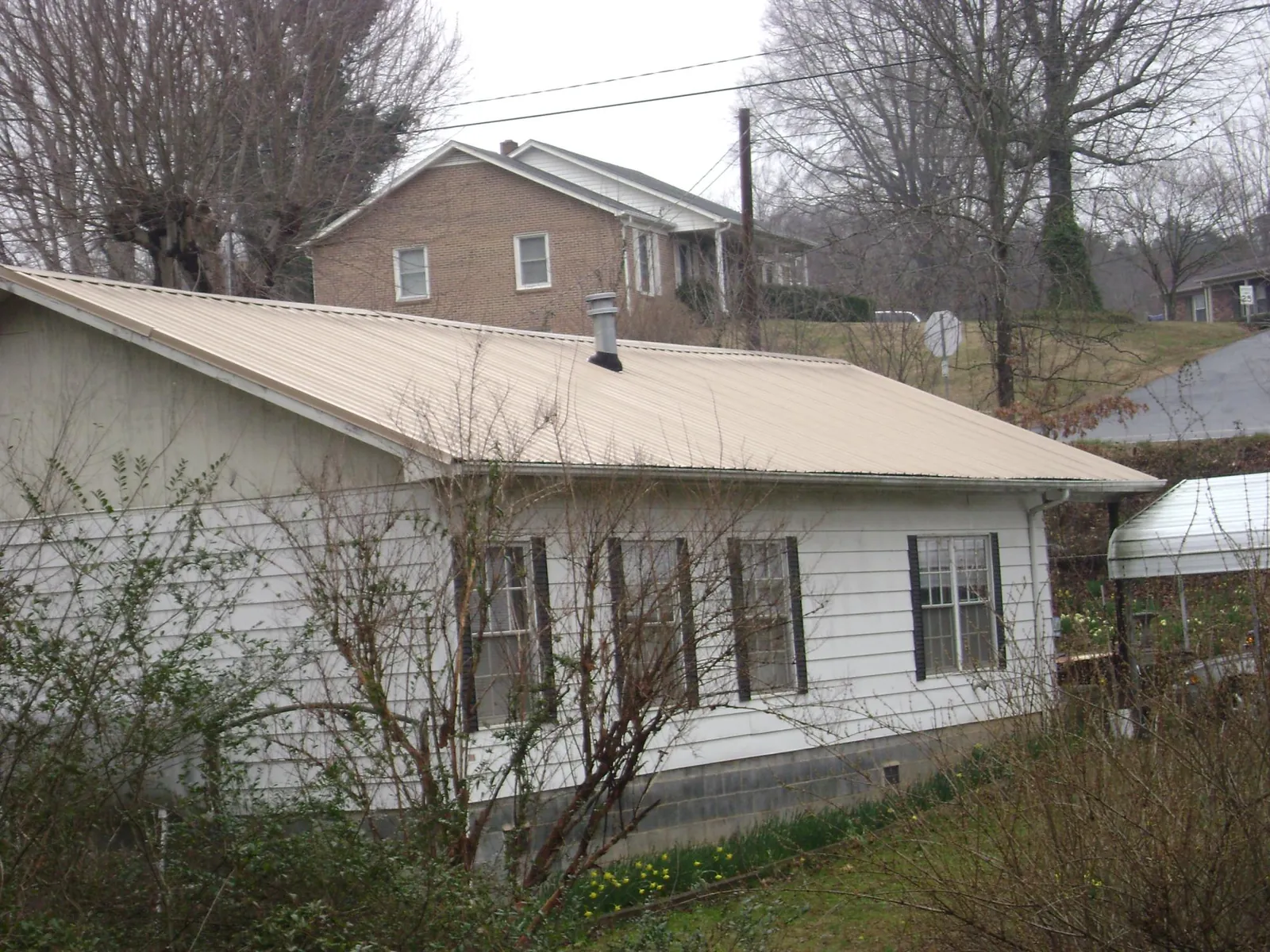 Tan metal roof on a white sided house set into a hillside — Commercial Roofing by Roofing Brothers in Valley Center